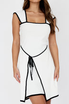 Woman wearing the Wimbledon White Contrast Trim Mini Dress with black piping detail, square neckline and tie waist.