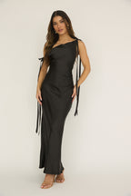 Woman wearing the Valentina Black Satin Asymmetric Maxi Dress featuring a one-shoulder neckline and elegant tie details, perfect for formal events and weddings.
