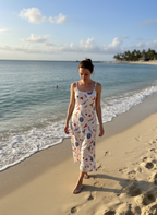 Woman wearing a white seashell print midi dress walking along a tropical beach at sunset.